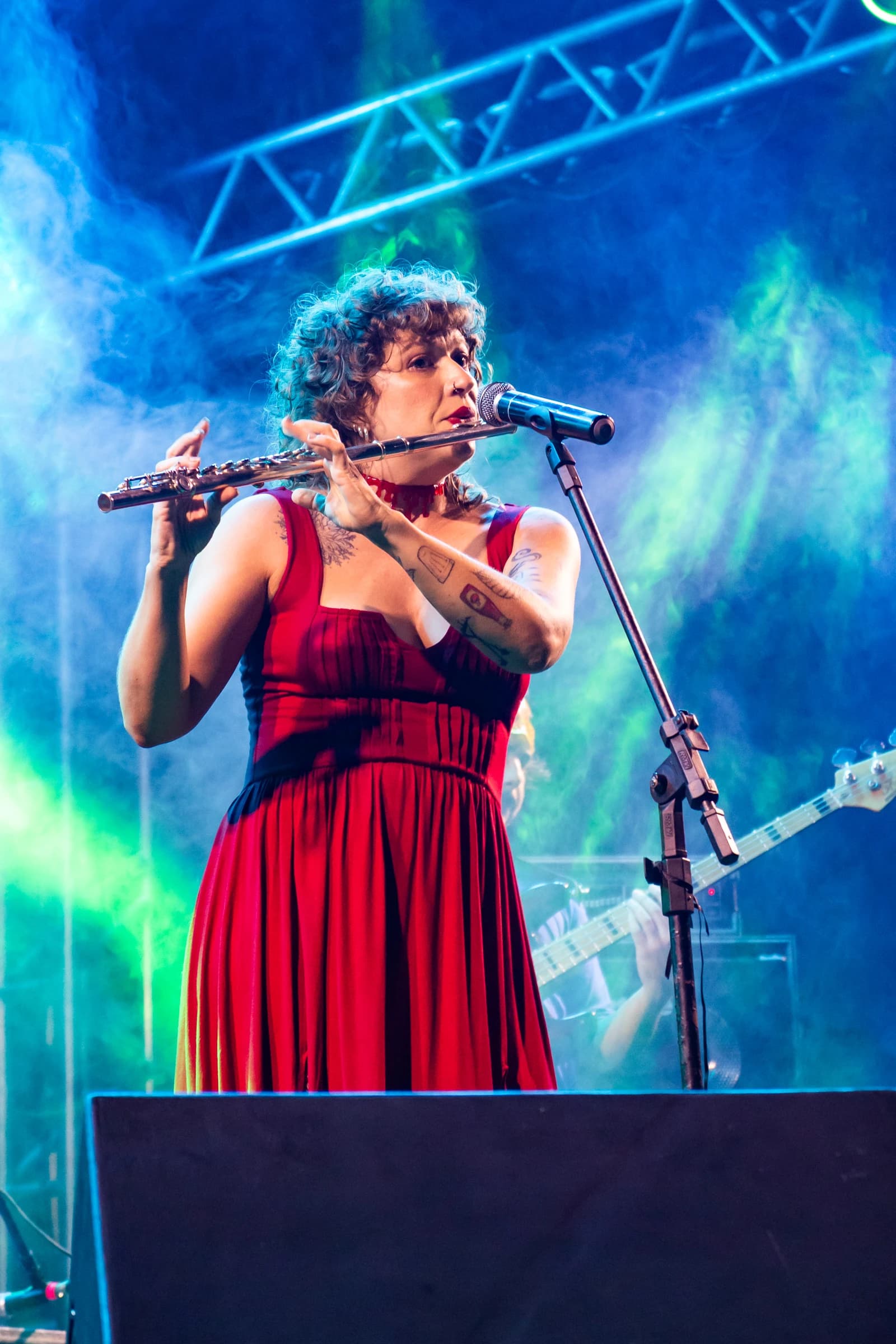Musicista de vestido vermelho toca flauta transversal sob luz azul.