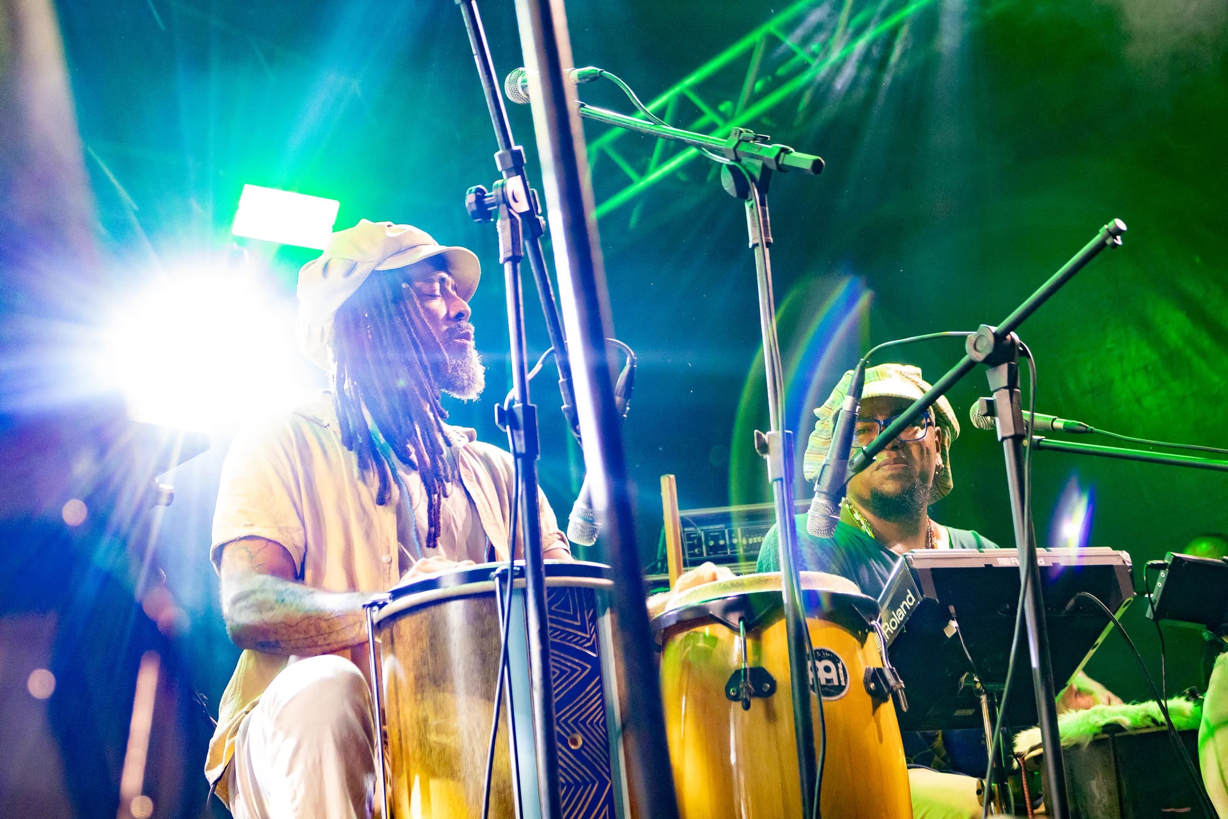 Percussionista toca tambores altos sob refletores brancos e verdes.