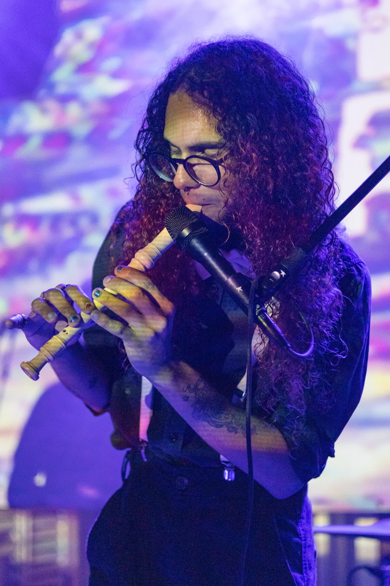 Artista de óculos toca um instrumento de sopro perto do microfone.
