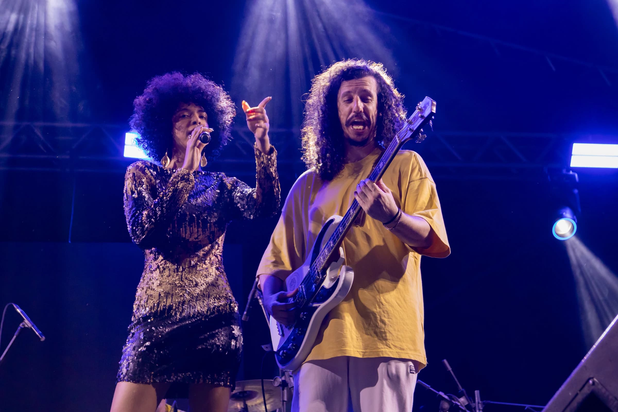 Vocalista e guitarrista dividem a apresentação, iluminados por luz azul.